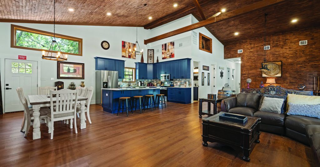 Fully equipped kitchen with blue cabinets and island bar seating next to a white dining set, overlooking the comfortable leather seating area in the main living space.