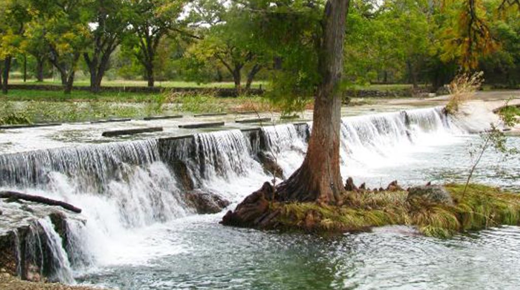 Cypress Falls Swimming Hole waterfall with tree roots and calm pool.